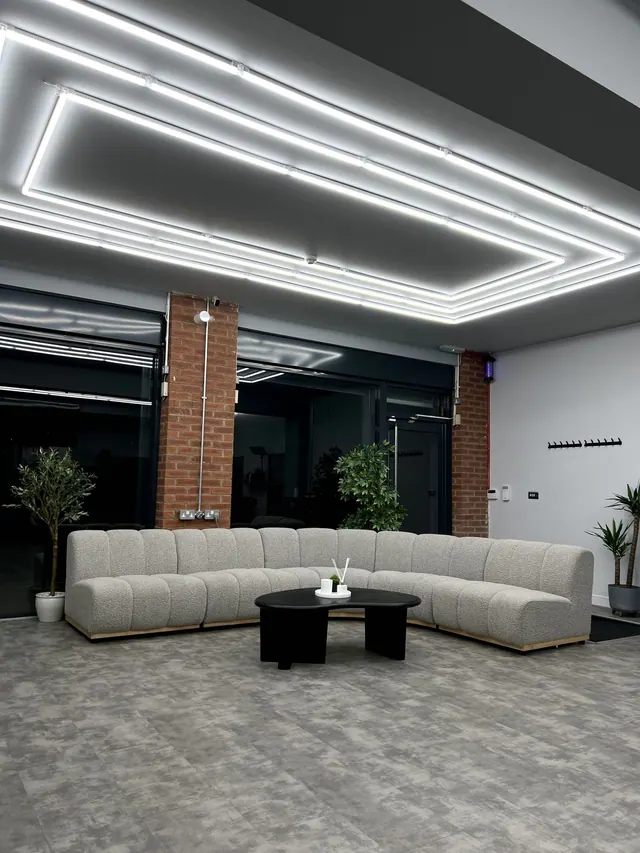 The lounge: a curved grey sofa and a round table under strip lighting